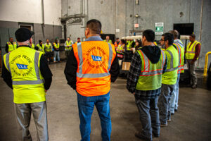 ILA union members are standing in a circle wearing safety vests and participating in a ILA Safety Meeting